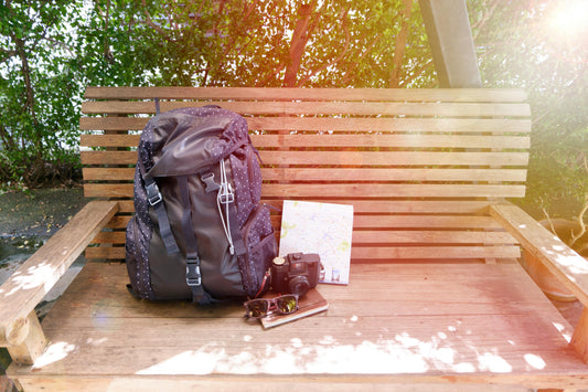 Polka-dot travel backpack with a camera, map, and sunglasses on an outdoor bench