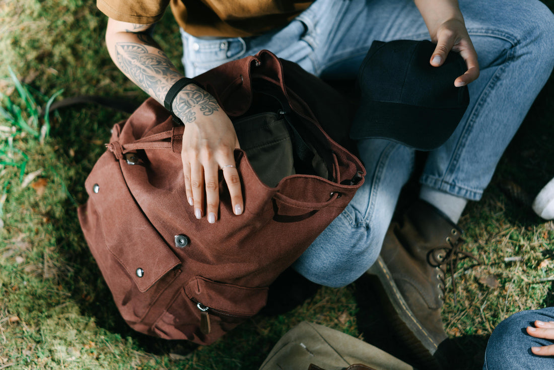 Overhead view of a hand unpacking a brown canvas backpack on grass