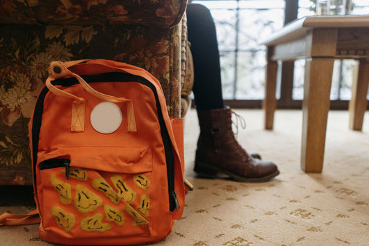 Custom-designed orange backpack with hand-painted patches resting against an armchair