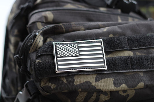 Camouflage tactical backpack with a black and white US flag patch, representing mil-spec MOLLE gear