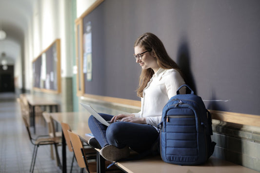 Person working on a laptop next to a backpack, illustrating tech-integrated smart backpacks