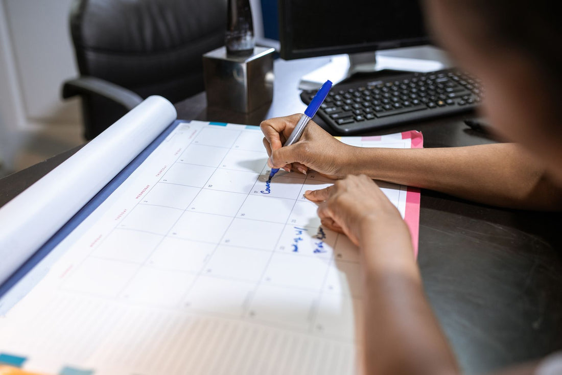Close-up of a hand writing an appointment on a desk calendar, evoking the order-timing decisions this guide works through.