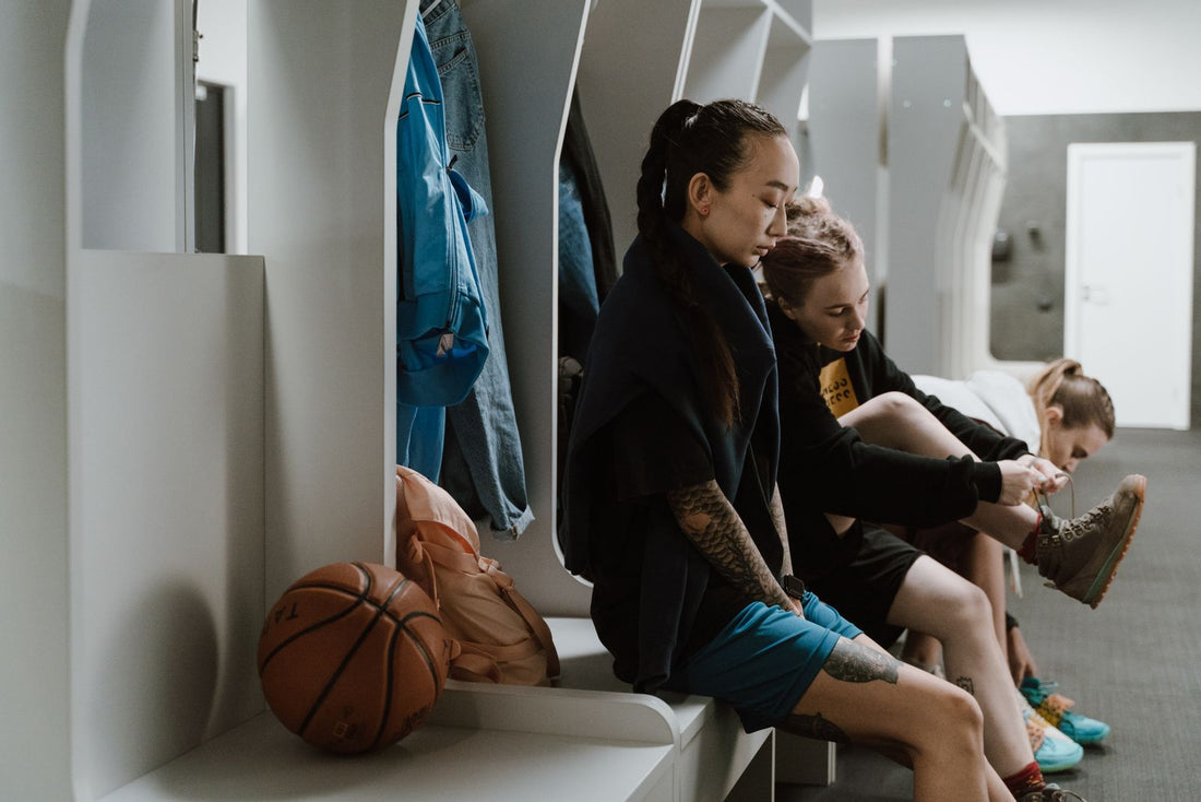 Women's basketball team preparing in the locker room, tying shoes and organizing sports gear before practice