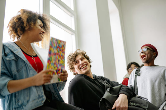 Group of college students laughing together in a bright hallway, one carrying a backpack